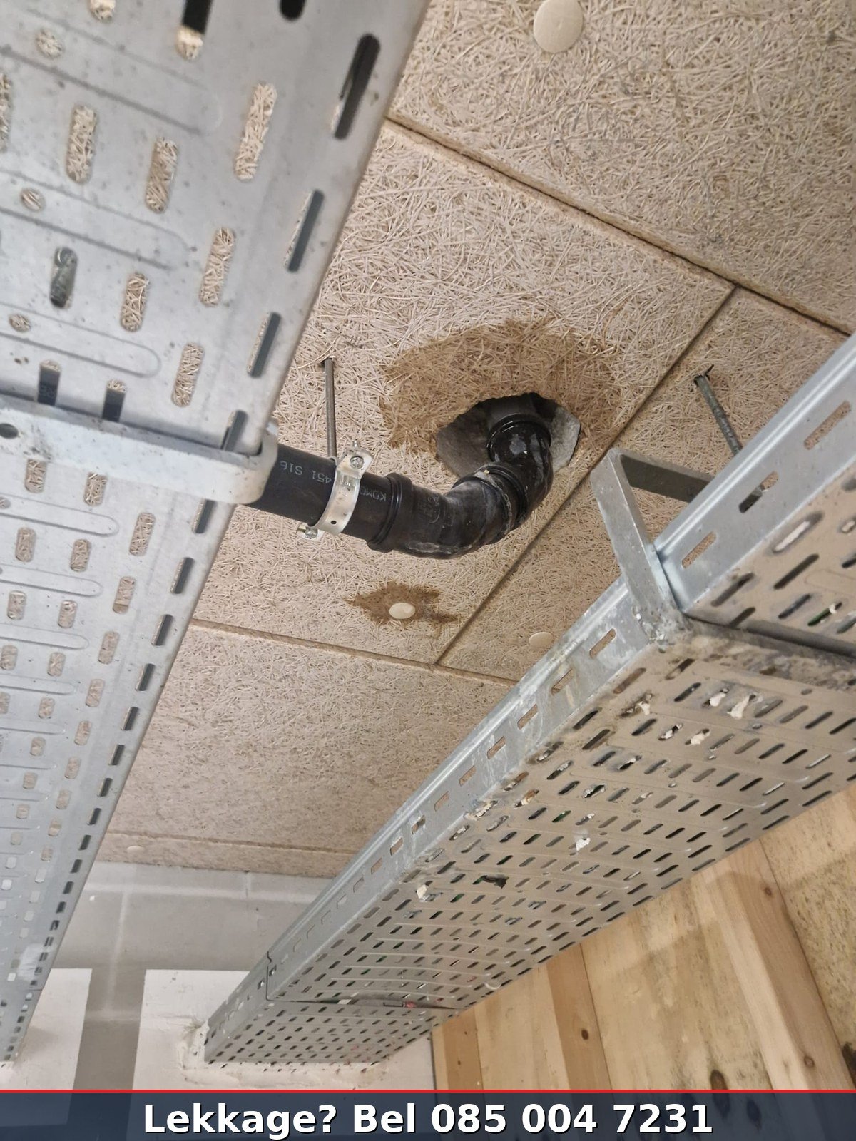 Lekkende afvoerpijp door systeemplafond bedrijfsruimte — vochtplekken op plafondtegels zichtbaar